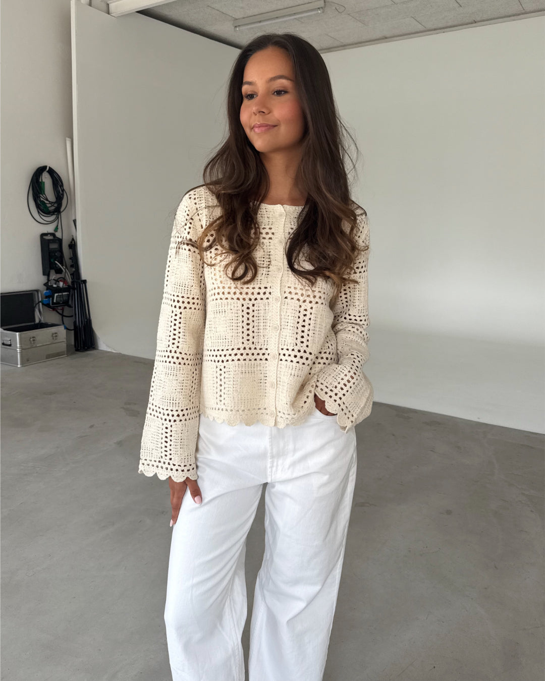 Modelfoto af pige som bærer en cremefarvet ORELLA cardigan med knapper, samt hvide jeans. Alt er fra BySofieSønderby