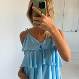En person i en lyseblå, flæset top tager en selfie med en grøn telefon i et lyst rum med en tavle i baggrunden.