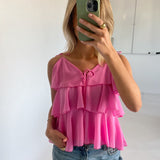Person tager et spejlbillede med en grøn telefon, iført en lyserød top med flæser og lyse jeans. Bagved er der en hvid væg og et whiteboard.