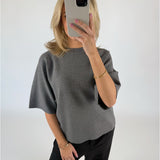 En person i gråt tøj tager et spejlbillede og holder en smartphone. Personen har blondt hår og et armbånd. Baggrunden er ensfarvet lys.