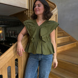 Kvinde står på trappe, iført en grøn bluse og blå jeans. Hun hviler hånden på gelænderet i en moderne, træinteriørindretning med dæmpet belysning.