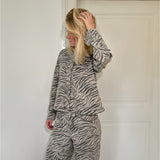 En person iført et zebra-mønstret sæt tøj står med hånden i håret foran en hvid dør i et minimalistisk rum.