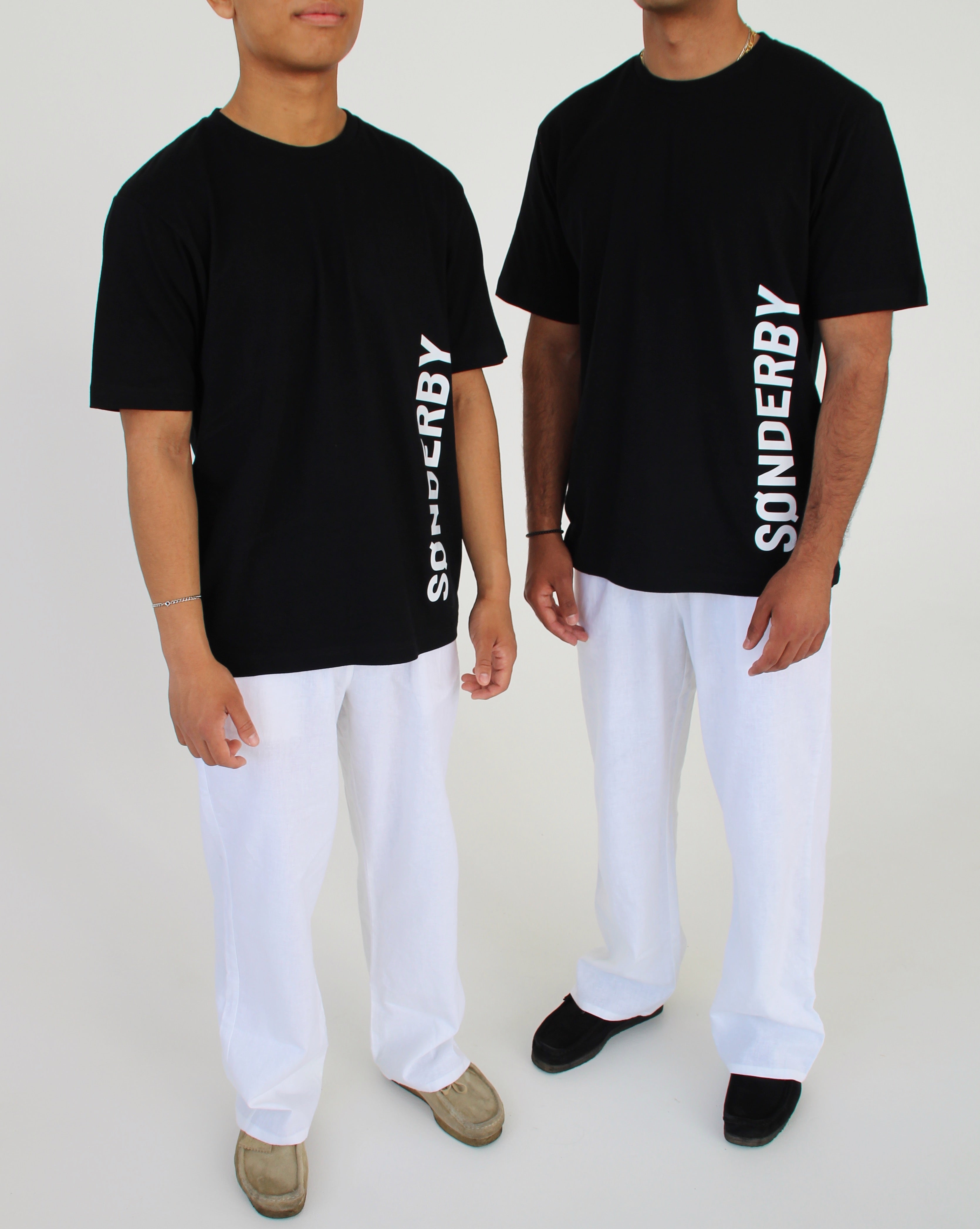 To mænd står i sort T-shirt med teksten "SØNDERBY" og hvide bukser. De står i et enkelt, hvidt rum.
