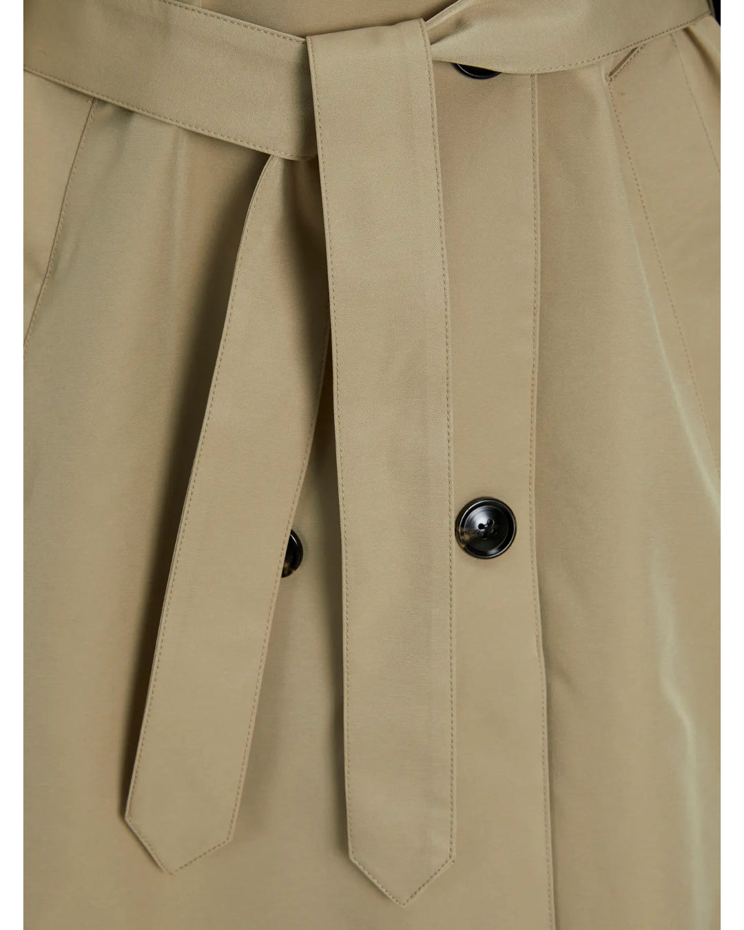 Beige trench coat med bælte, der hænger løst foran. To sorte knapper fastgør stoffet på hver side. Baggrunden er neutral, hvilket fremhæver tøjet.
