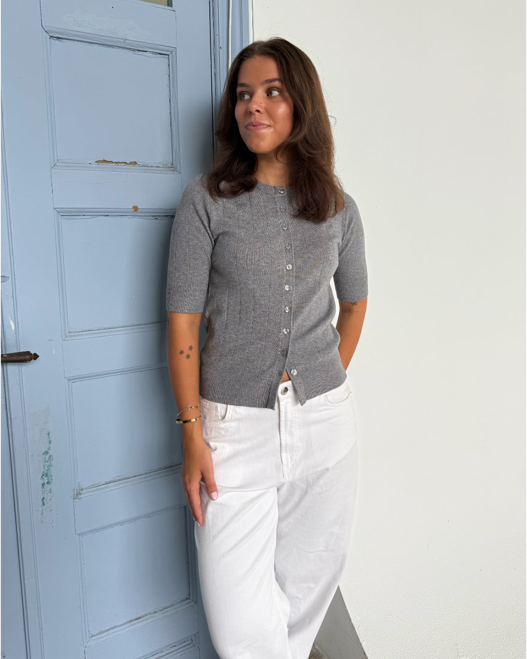 Modelfoto af pige som bærer en Spina cardigan i grå, samt et par hvide Nanna jeans. Alt fra By Sofie Sønderby