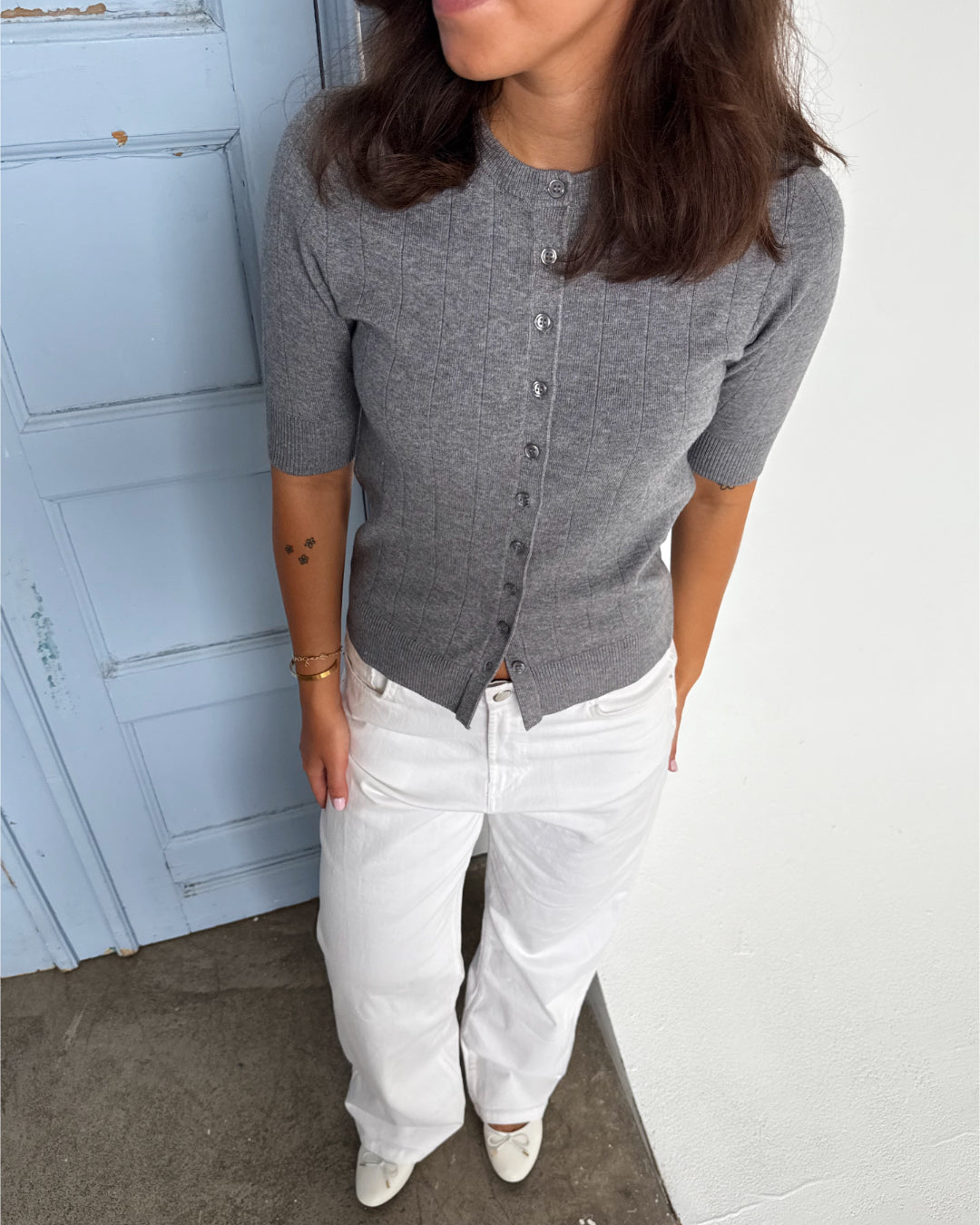 Modelfoto af pige som bærer en Spina cardigan i grå, samt et par hvide Nanna jeans. Alt fra By Sofie Sønderby