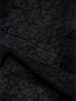 Sort blonderstof foldet med blomstermønster, der danner en delikat tekstur. Stoffet ligger fladt i et neutraliseret lys.