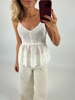 En person tager et spejlbillede iført en hvid hæklet top og lyse bukser, mens de holder en mørkerød mobiltelefon. Baggrunden er simpel og lys.