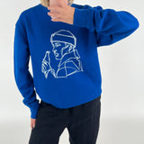 En person iført en blå sweatshirt med en hvid, stiliseret tegning af en person der holder en flaske, tager et spejlbillede i et lyst rum.