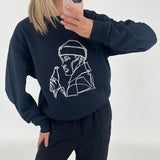 En person tager et spejlbillede iført en sort sweatshirt med en line-tegning af en person med en drikkeflaske. Baggrunden er neutral og lys.