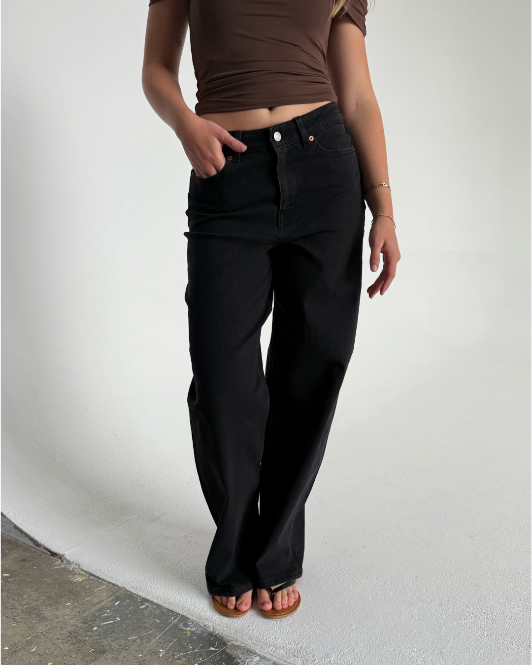 Modelfoto af pige som bærer et par sorte Tokyo jeans, samt iført en brun Thora top og sorte Carmen sandaler. Alt fra By Sofie Sønderby