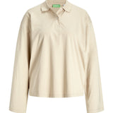 Beige langærmet poloshirt med krave og knaplukning foran. Etiket med teksten "AJXX" inde i nakken. Ingen synlig handling eller særlige omgivelser.