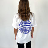En person iført en hvid t-shirt med et blåt globusmotiv og teksten "WORLDWIDE" står med ryggen til kameraet i et neutralt, lyst rum.