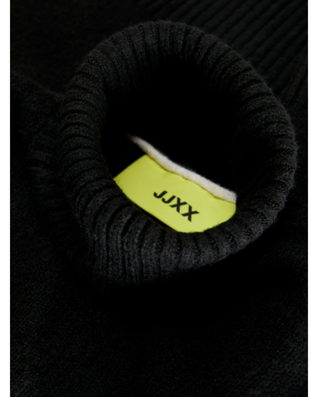 En sort ribstrikket rullekrave sweater viser etiketmærket med teksten "JJXX" inde i halsudskæringen.