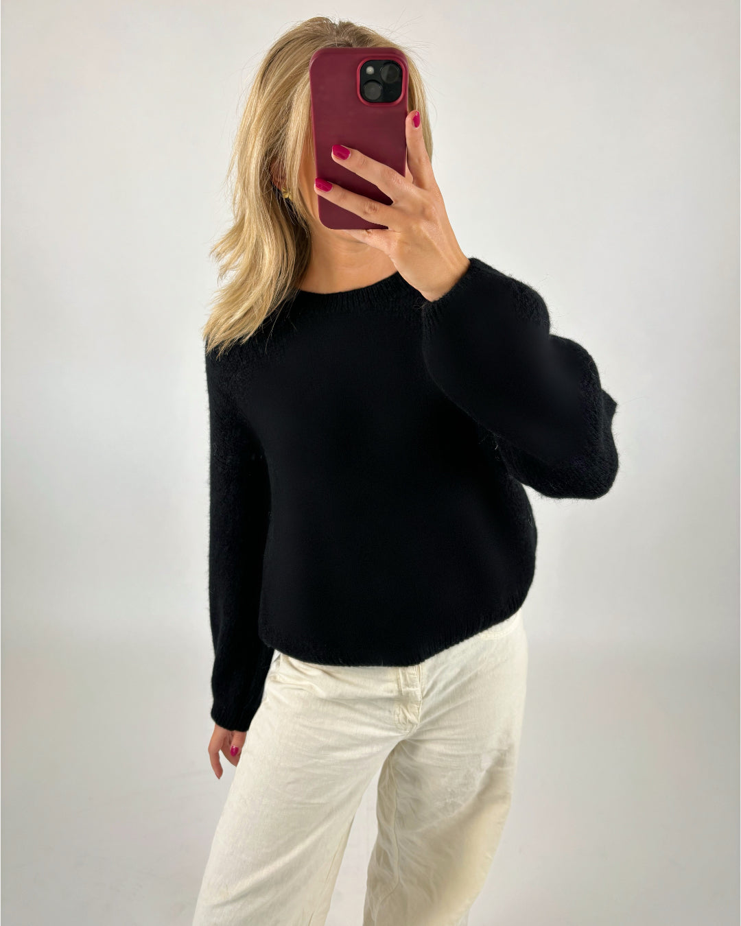 En person iført en sort trøje og hvide bukser tager et billede med en mobiltelefon i et minimalistisk rum.