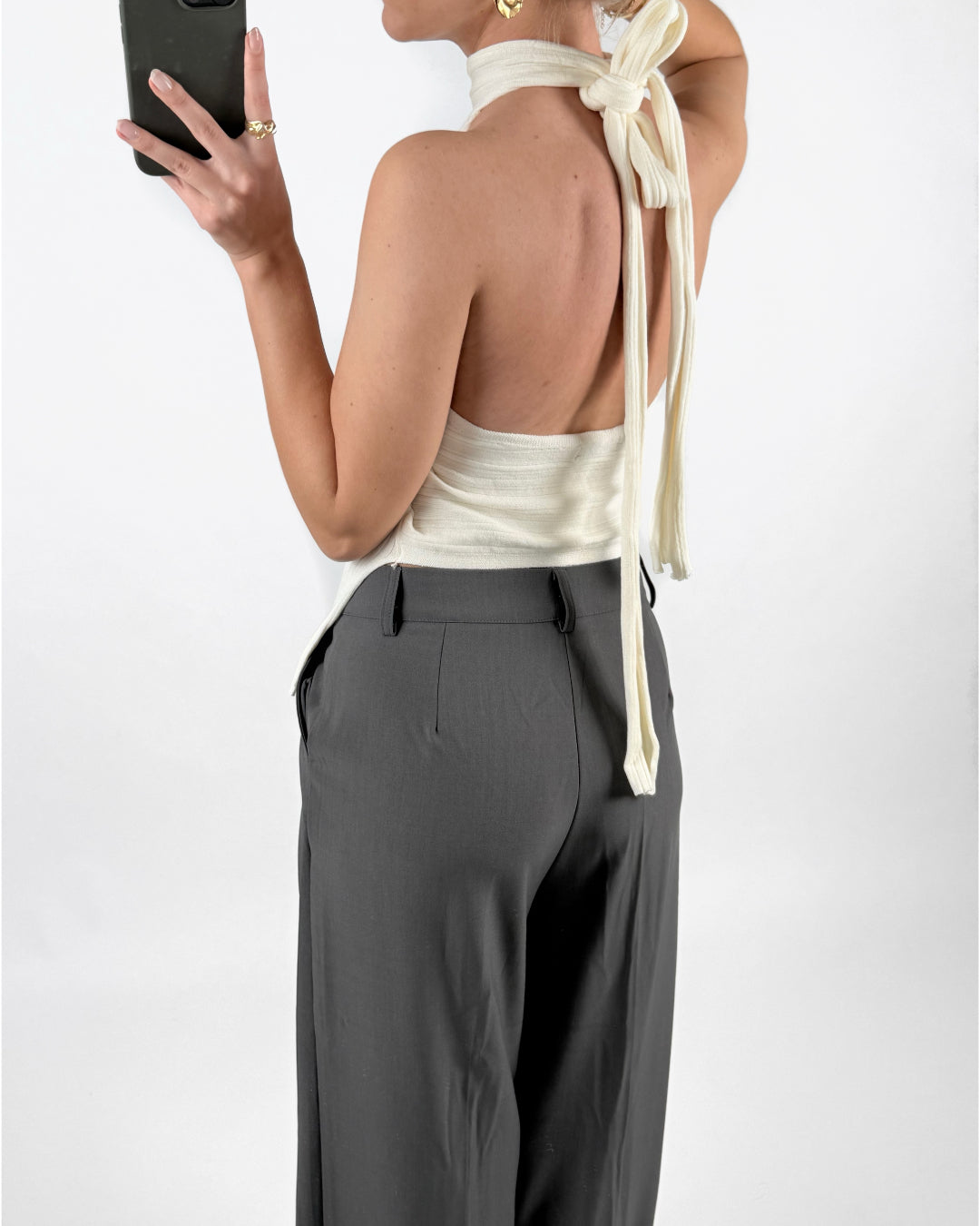 Modelfoto af pige med cremefarvet ASHLYN halterneck top, samt grå MILAN bukser. Set bagfra. Alt er fra BySofieSønderby