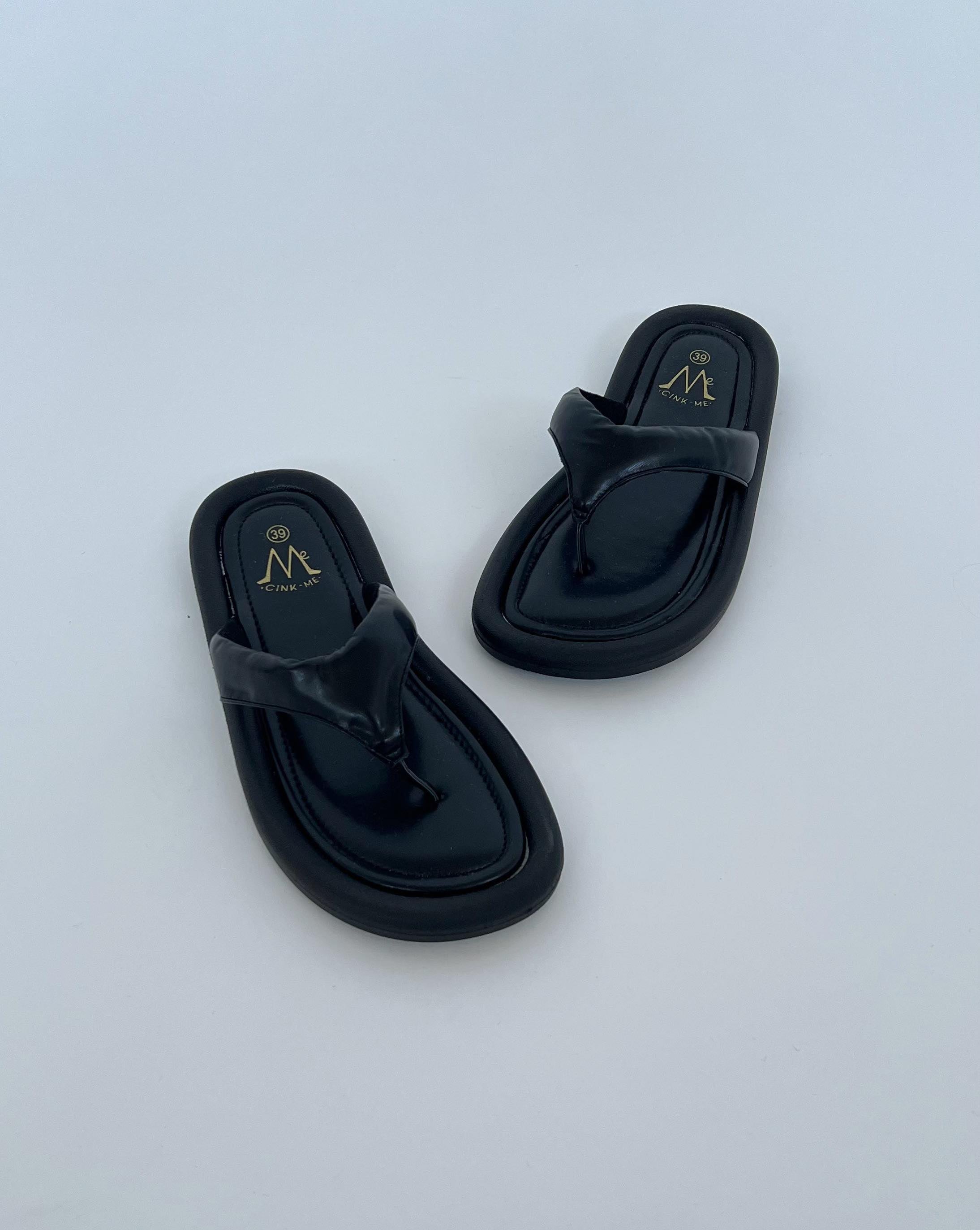 Sorte sandaler ligger på en hvid overflade. Teksten "39" og "CINK ME" er trykt i guld på indersålen.