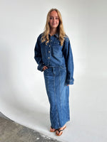 Modelfoto af pige som bærer en blå Cana denim jakke, samt Cana denim nederdel og sorte Carmen sandaler. Alt fra By Sofie Sønderby