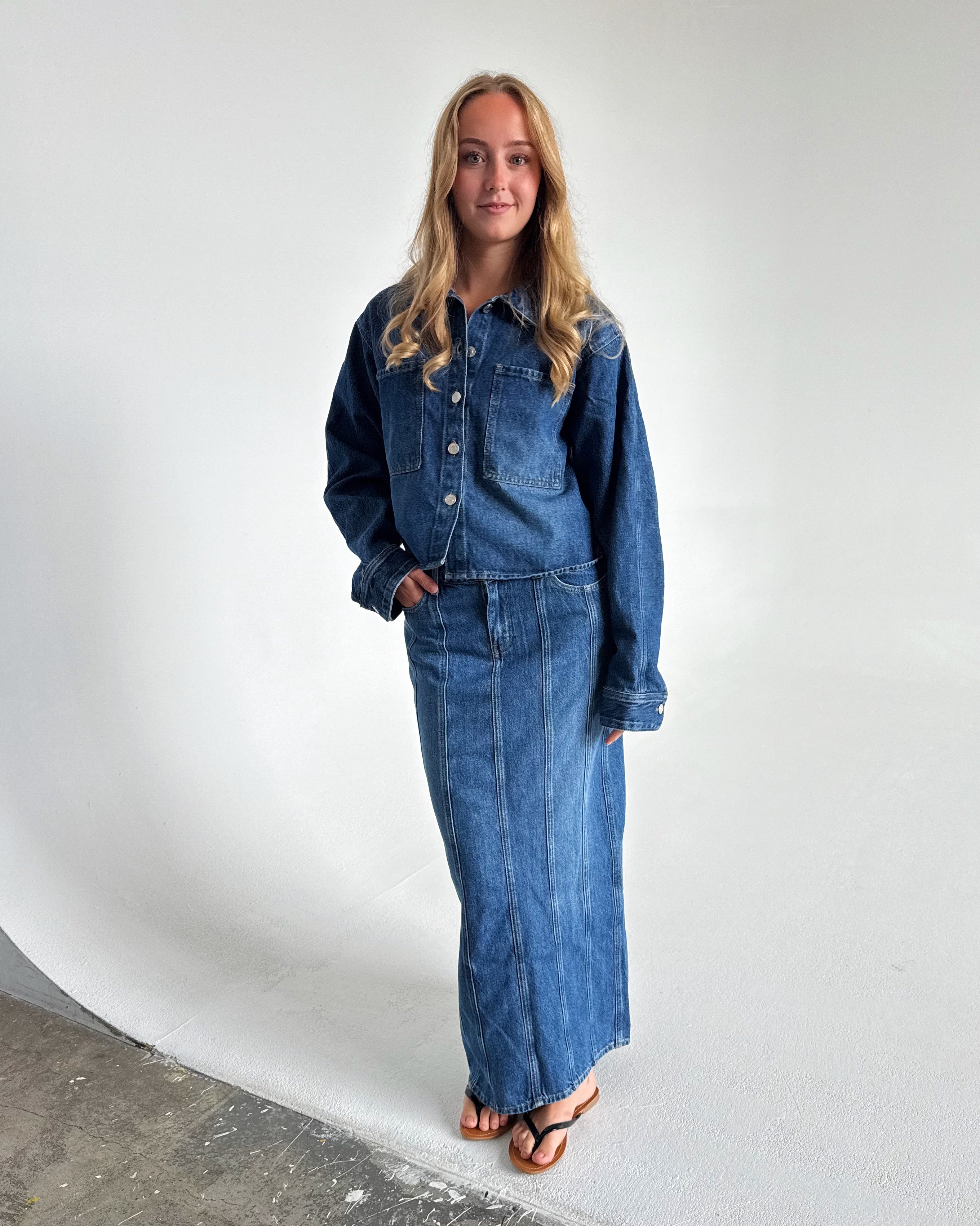 Modelfoto af pige som bærer en blå Cana denim jakke, samt Cana denim nederdel og sorte Carmen sandaler. Alt fra By Sofie Sønderby