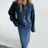 Modelfoto af pige som bærer en blå Cana denim jakke, samt Cana denim nederdel og sorte Carmen sandaler. Alt fra By Sofie Sønderby