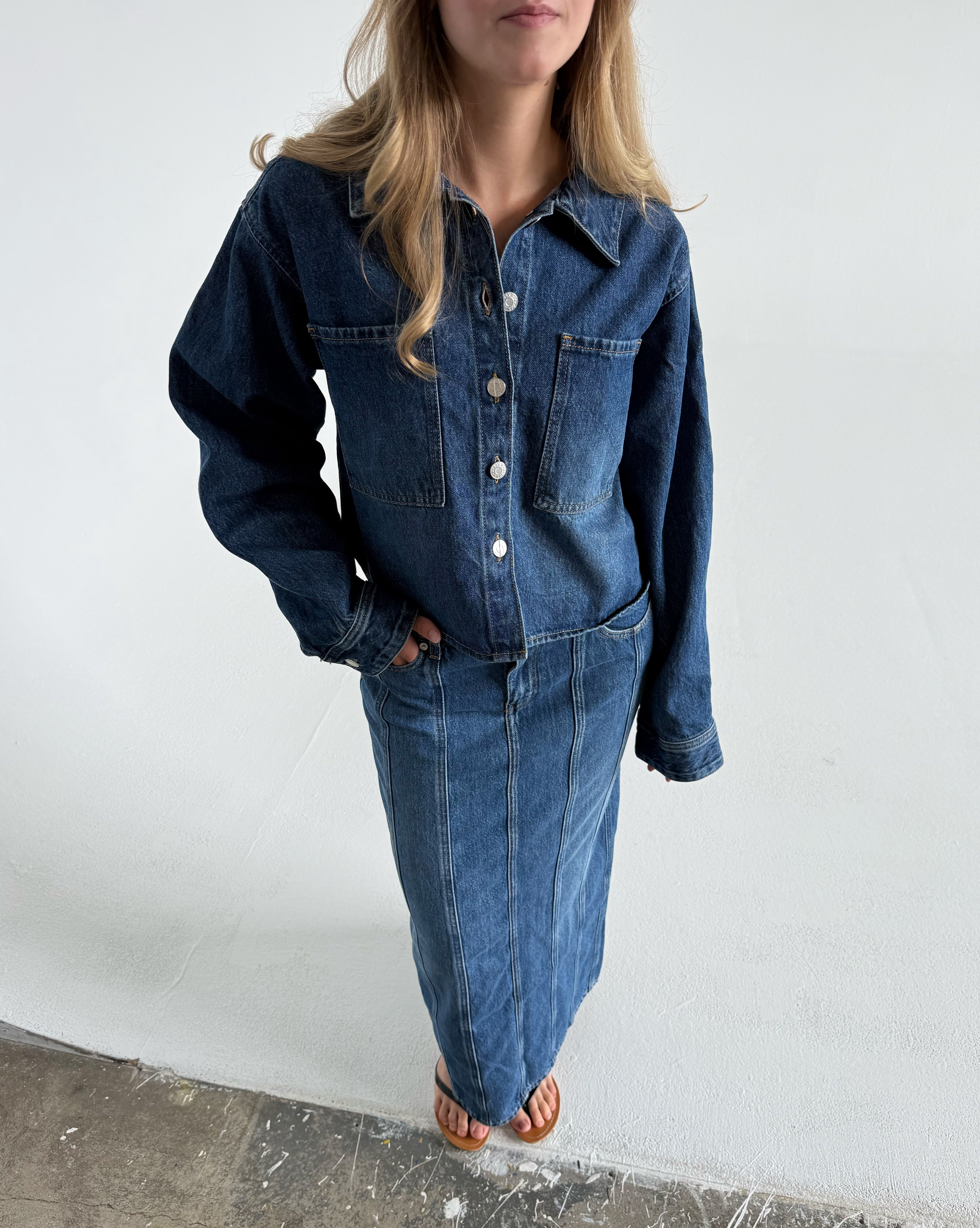 Modelfoto af pige som bærer en blå Cana denim jakke, samt Cana denim nederdel og sorte Carmen sandaler. Alt fra By Sofie Sønderby