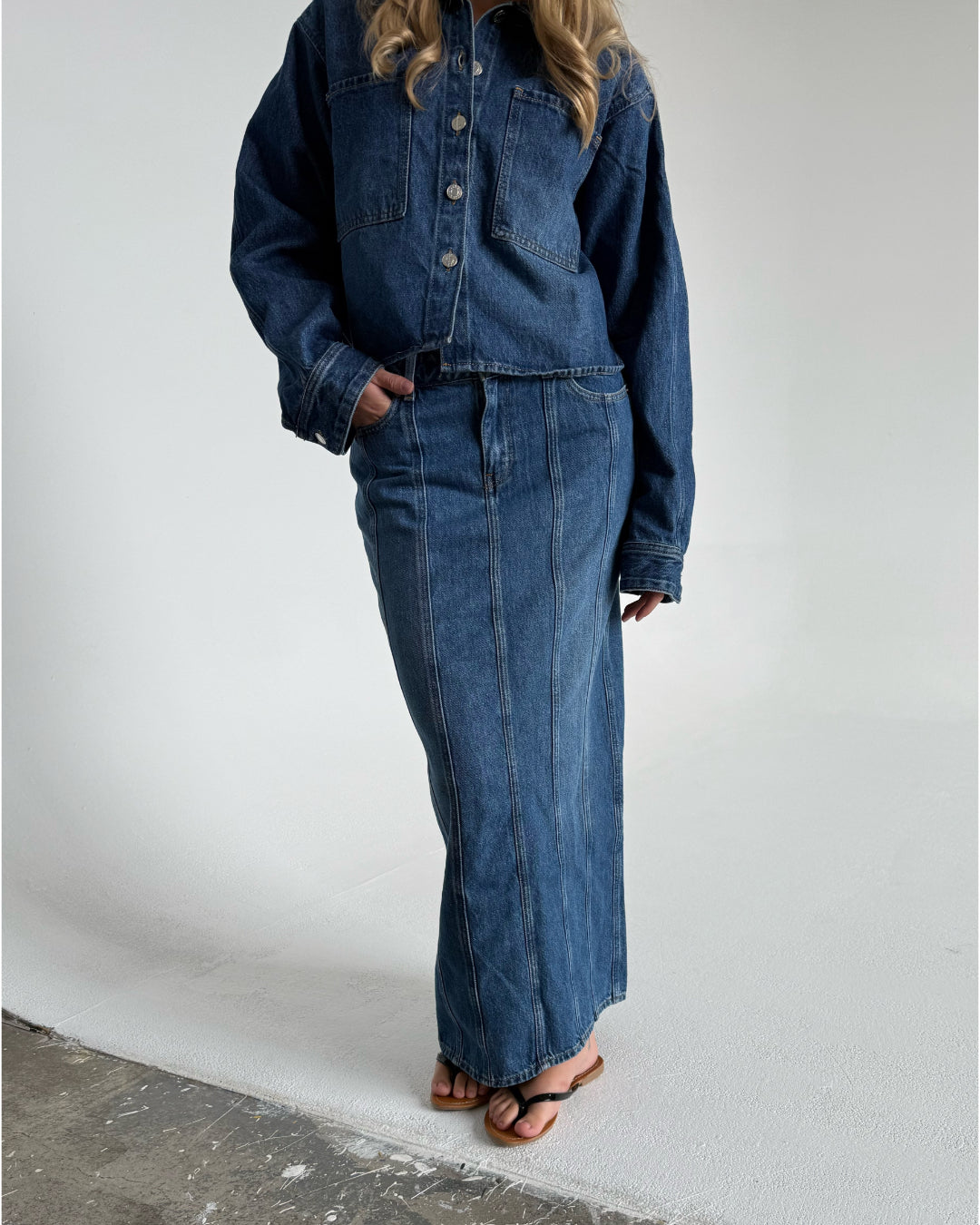 Modelfoto af pige som bærer en blå Cana denim nederdel, samt Cana denim jakke og sorte Carmen sandaler. Alt fra By Sofie Sønderby