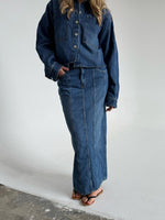 Modelfoto af pige som bærer en blå Cana denim nederdel, samt Cana denim jakke og sorte Carmen sandaler. Alt fra By Sofie Sønderby