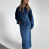 Modelfoto af pige som bærer en blå Cana denim nederdel, samt Cana denim jakke og sorte Carmen sandaler. Alt fra By Sofie Sønderby