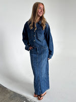 Modelfoto af pige som bærer en blå Cana denim nederdel, samt Cana denim jakke og sorte Carmen sandaler. Alt fra By Sofie Sønderby