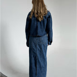Modelfoto af pige som bærer en blå Cana denim nederdel, samt Cana denim jakke og sorte Carmen sandaler. Alt fra By Sofie Sønderby