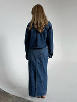 Modelfoto af pige som bærer en blå Cana denim nederdel, samt Cana denim jakke og sorte Carmen sandaler. Alt fra By Sofie Sønderby