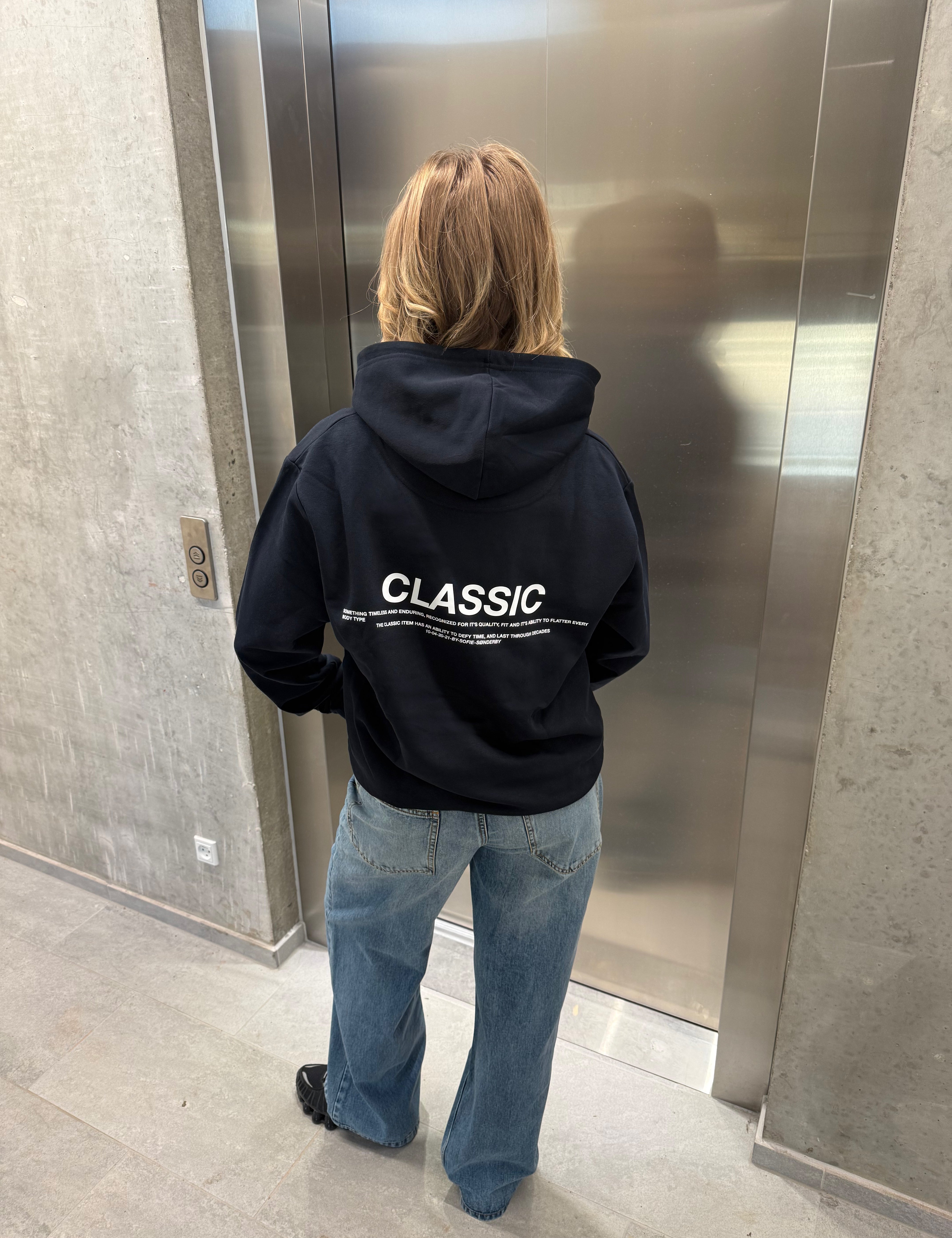 Stemningsbillede af pige der bærer en navy hoodie med hvidt classic tryk og blå NANNA jeans.  Fra BySofieSønderby