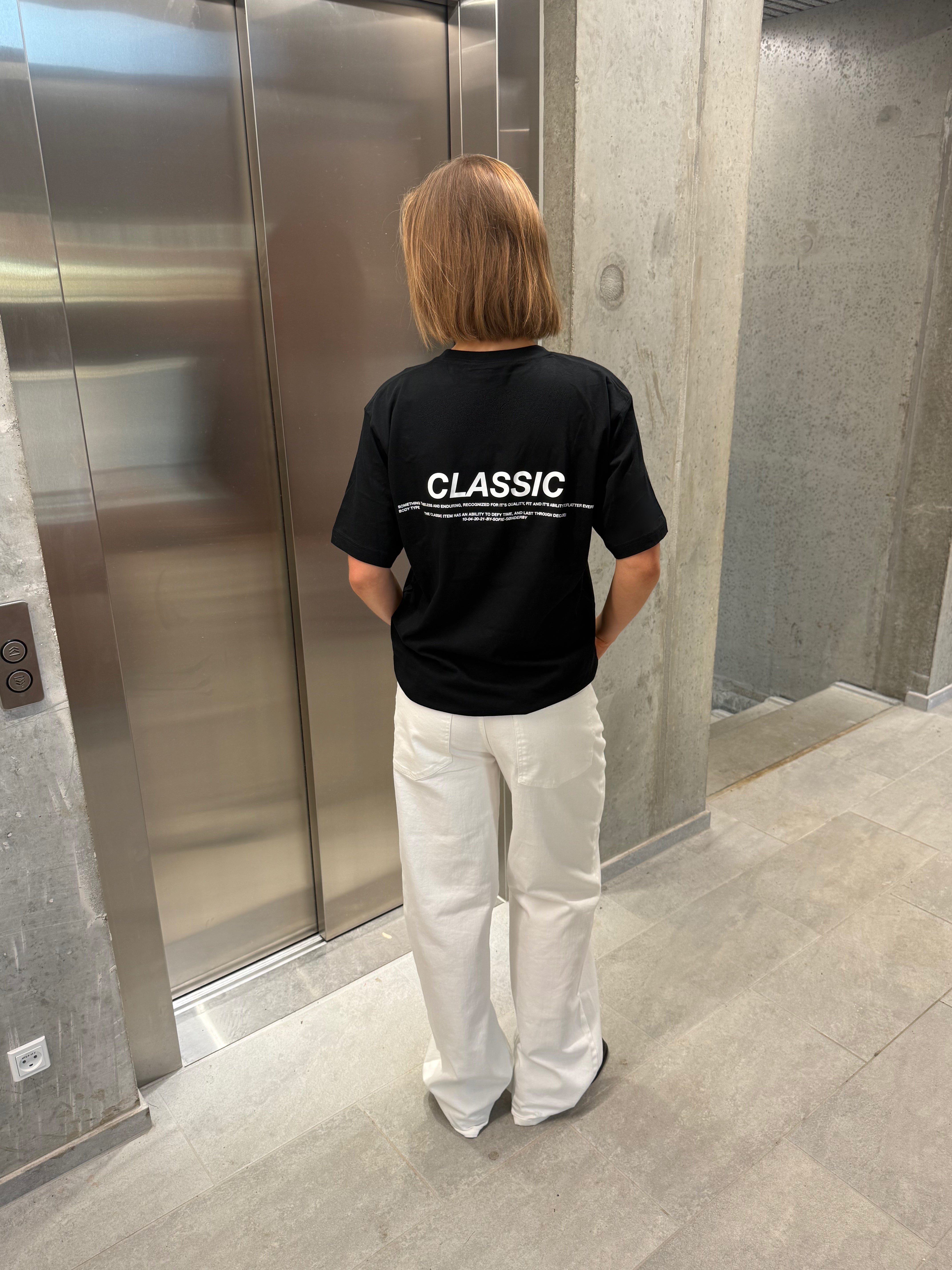 Stemningsbillede af pige der bærer en sort t-shirt med hvidt classic tryk og hvide NANNA jeans.  Fra BySofieSønderby