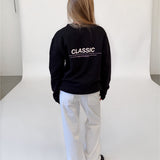 Modelfoto af pige i sort CLASSIC sweatshirt med reflekstryk, samt hvide NANNA jeans. Alt er fra BySofieSønderby.