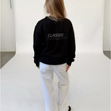 Modelfoto af pige i sort CLASSIC sweatshirt med reflekstryk, samt hvide NANNA jeans. Alt er fra BySofieSønderby.