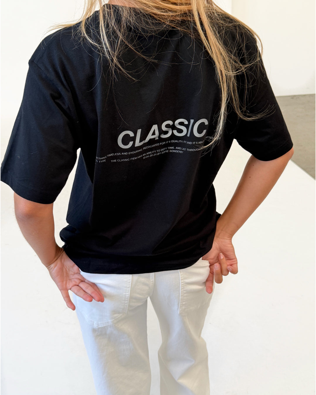 Modelfoto af pige i sort CLASSIC t-shirt med reflekstryk, samt hvide NANNA jeans. Alt er fra BySofieSønderby.