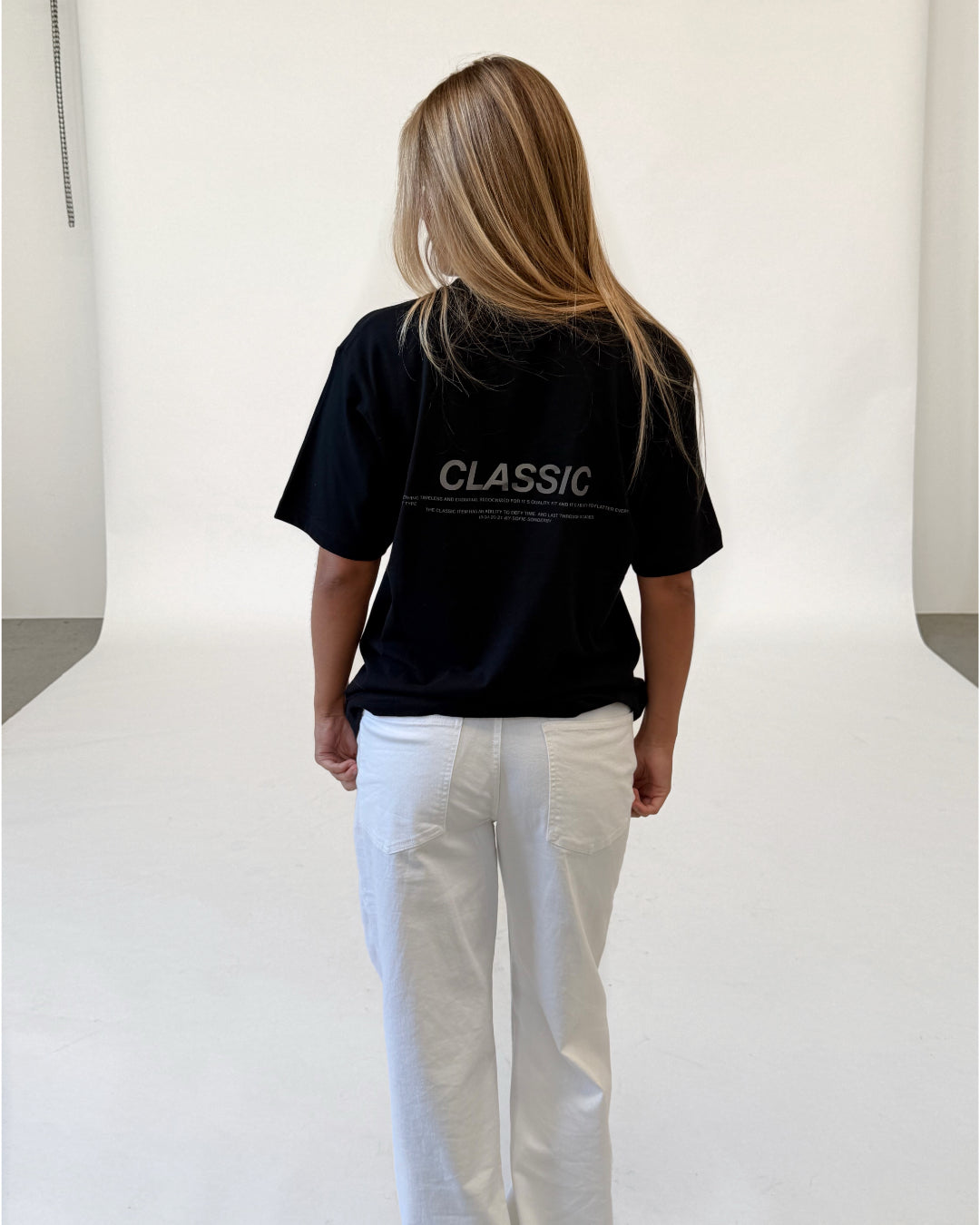 Modelfoto af pige i sort CLASSIC t-shirt med reflekstryk, samt hvide NANNA jeans. Alt er fra BySofieSønderby.