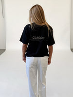 Modelfoto af pige i sort CLASSIC t-shirt med reflekstryk, samt hvide NANNA jeans. Alt er fra BySofieSønderby.