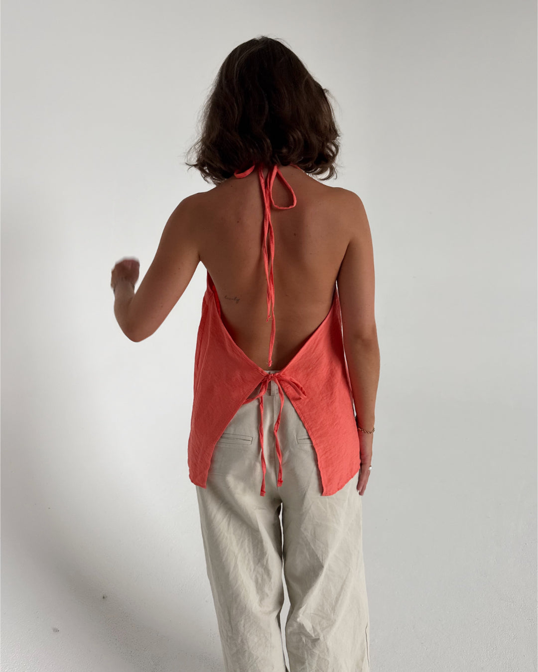 Modelfoto af pige som bærer en Daisy top i coral, samt et par beige Yale bukser. Alt fra By Sofie Sønderby