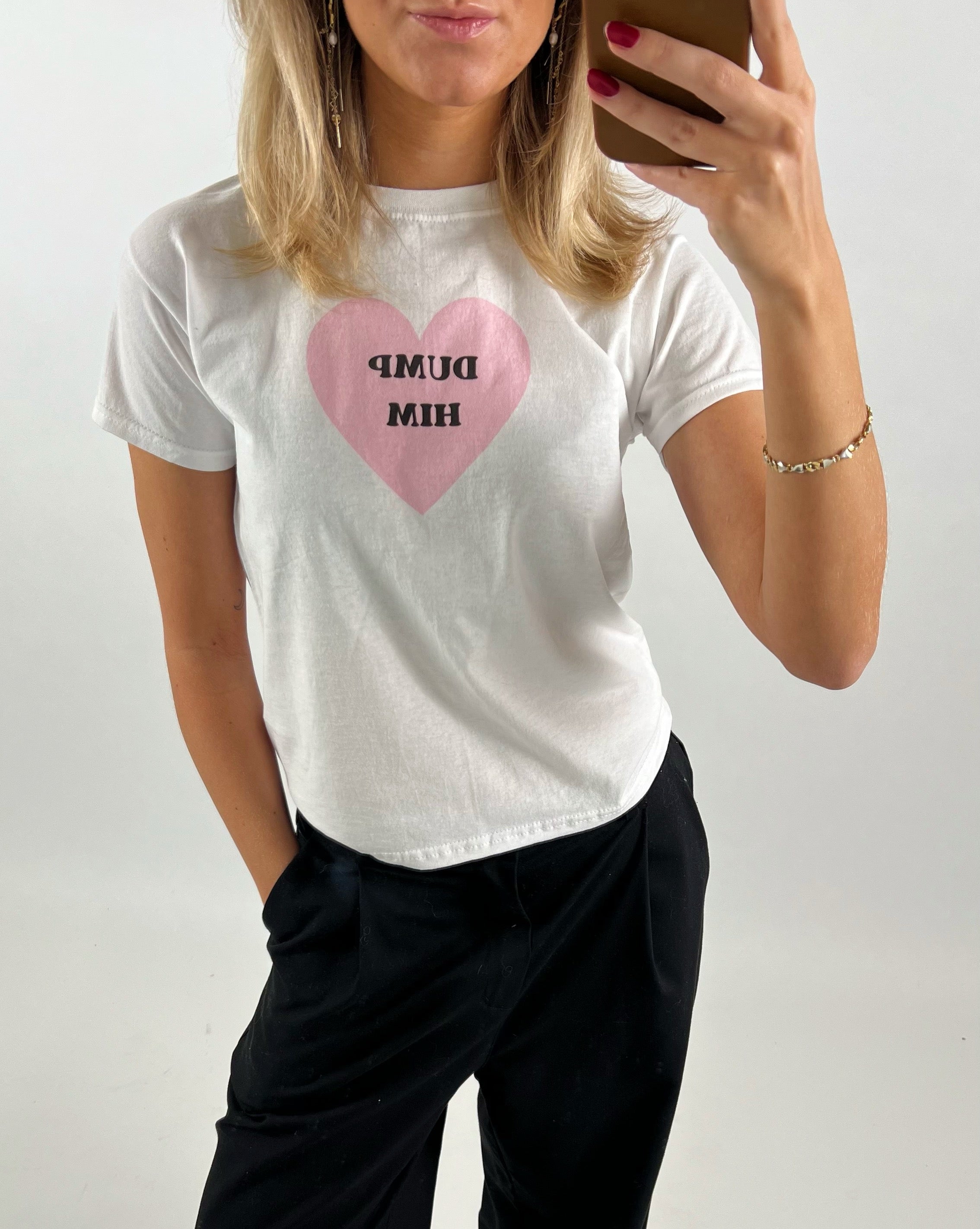 Kvinde tager selfie iført hvid t-shirt med lyserødt hjerte og teksten "DUMP HIM", mens hun står i et lyst rum.