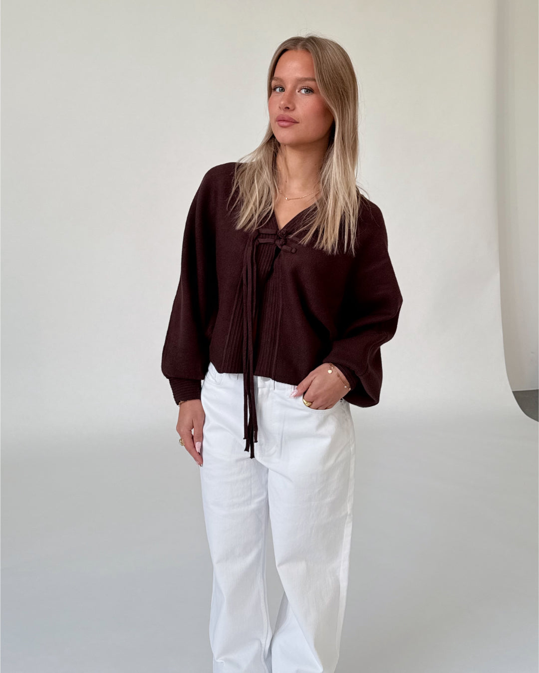 Modelfoto af pige i brun ELLIOT cardigan, samt hvide NANNA jeans. Alt er fra BySofieSønderby.