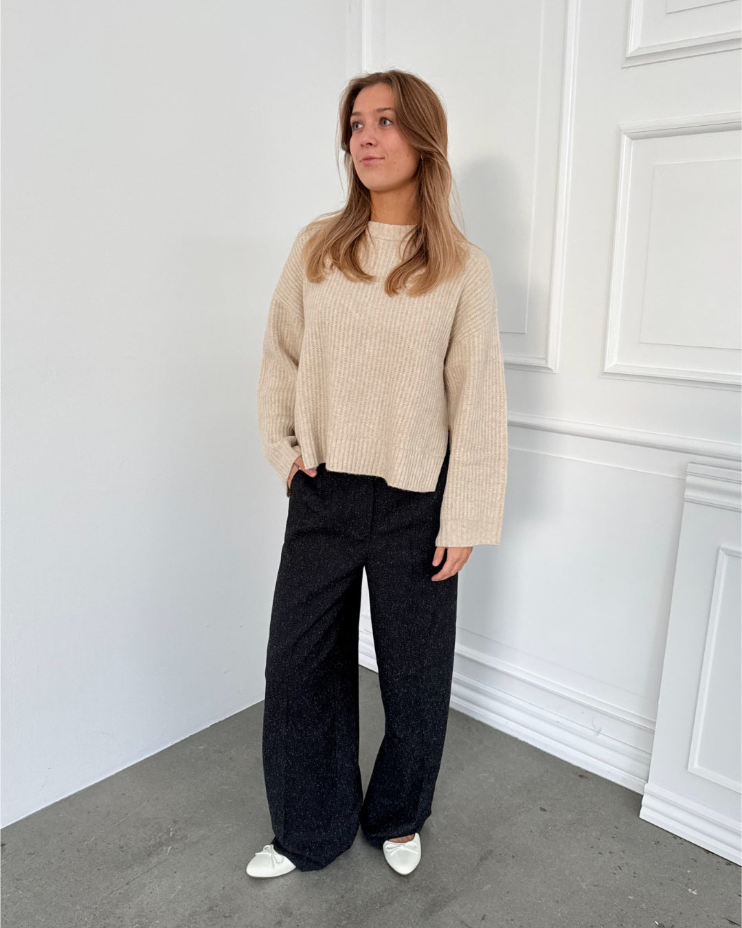 Modelfoto af pige i sort melerede ELLIS bukser, samt beige striktrøje. Alt er fra BySofieSønderby.