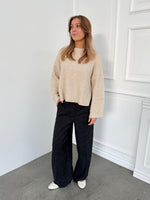 Modelfoto af pige i sort melerede ELLIS bukser, samt beige striktrøje. Alt er fra BySofieSønderby.