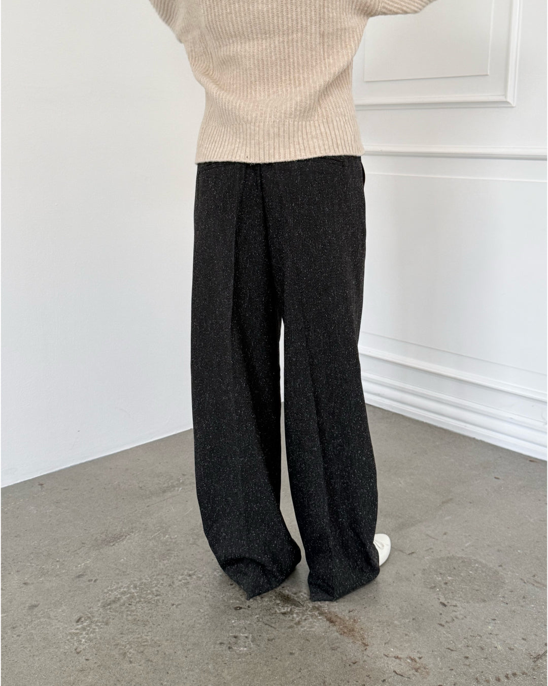 Modelfoto af pige i sort melerede ELLIS bukser, samt beige striktrøje. Alt er fra BySofieSønderby.