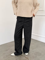 Modelfoto af pige i sort melerede ELLIS bukser, samt beige striktrøje. Alt er fra BySofieSønderby.