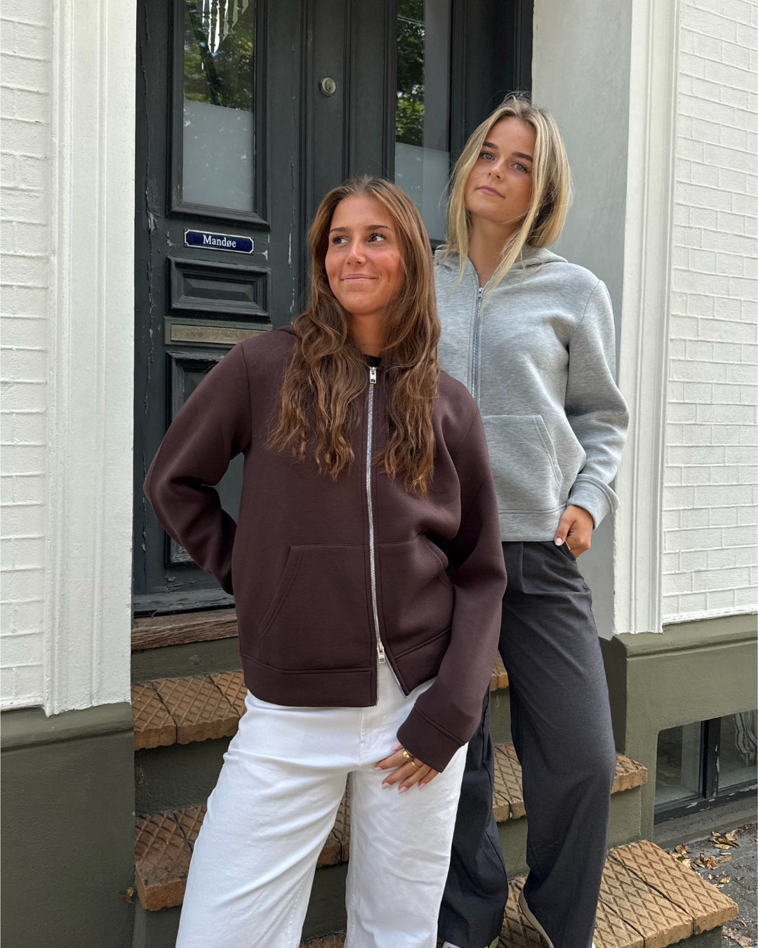 Modelfoto af 2 piger, som begge bærer en EMMA hoodie, brun og lysegrå. Dertil NANNA jeans, hvide og MILAN bukser, grå - alt fra BySofieSønderby