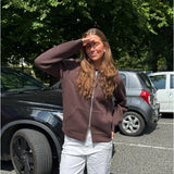 Modelfoto af pige, som bærer EMMA hoodie, brun og NANNA jeans, hvid - alt fra BySofieSønderby. Baggrund er p-plads og træer