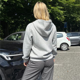 Modelfoto af pige, som bærer EMMA hoodie, lysegrå og MILAN bukser, grå - alt fra BySofieSønderby. Baggrund er p-plads og træer