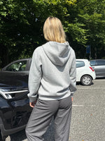 Modelfoto af pige, som bærer EMMA hoodie, lysegrå og MILAN bukser, grå - alt fra BySofieSønderby. Baggrund er p-plads og træer