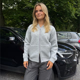 Modelfoto af pige, som bærer EMMA hoodie, lysegrå og MILAN bukser, grå - alt fra BySofieSønderby. Baggrund er p-plads og træer